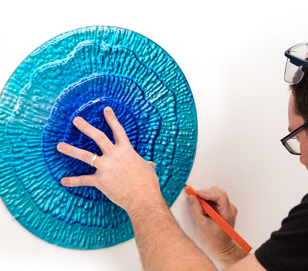Person marking placement on a blue acrylic wall display for installation.