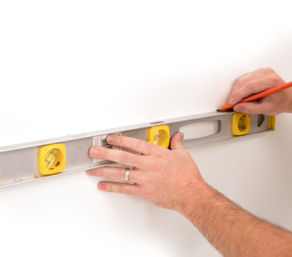 Person using a level and pencil to mark placement for wall hardware installation.