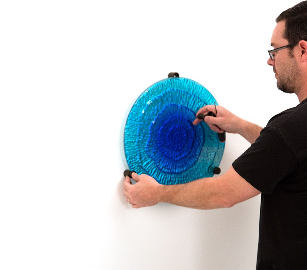 Person installing a blue acrylic wall display with standoff mounting hardware.