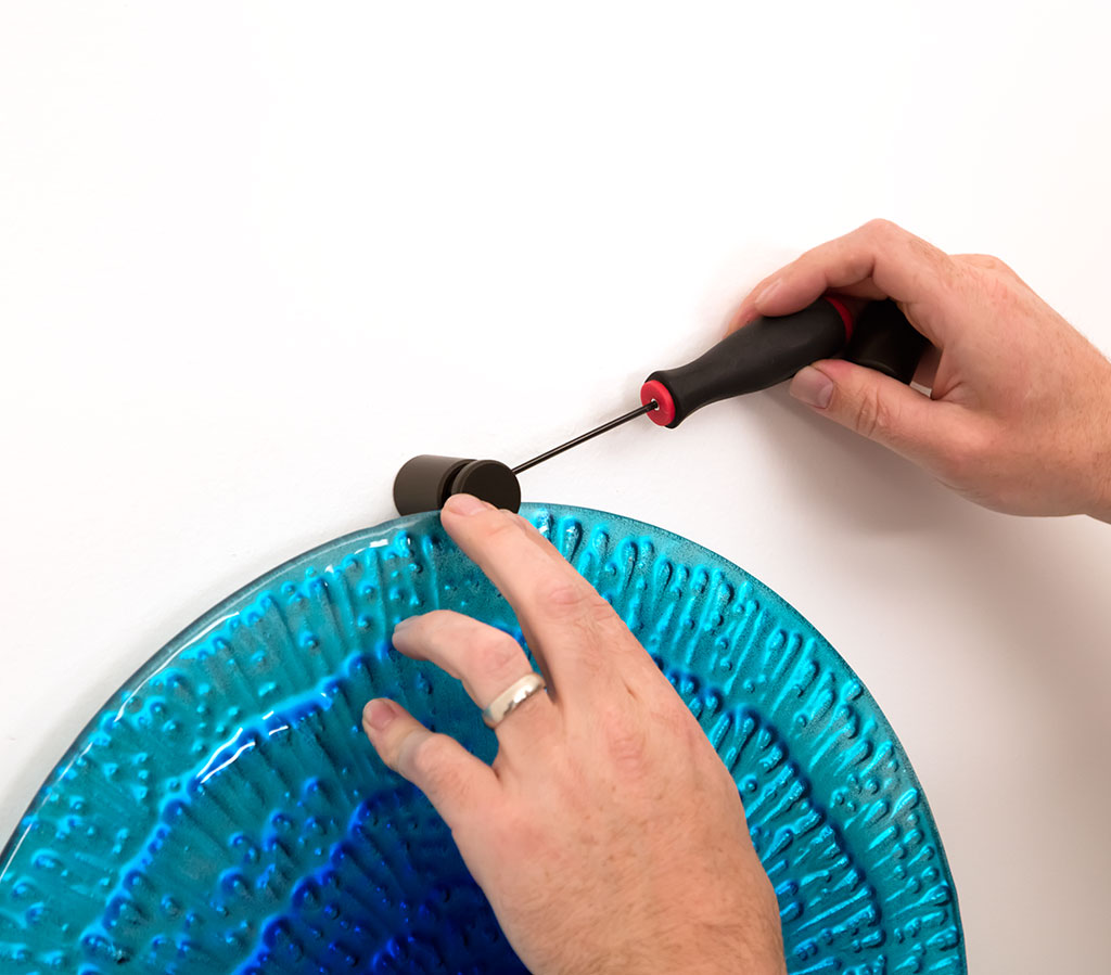 Person securing a blue acrylic wall display with standoff hardware using a screwdriver.