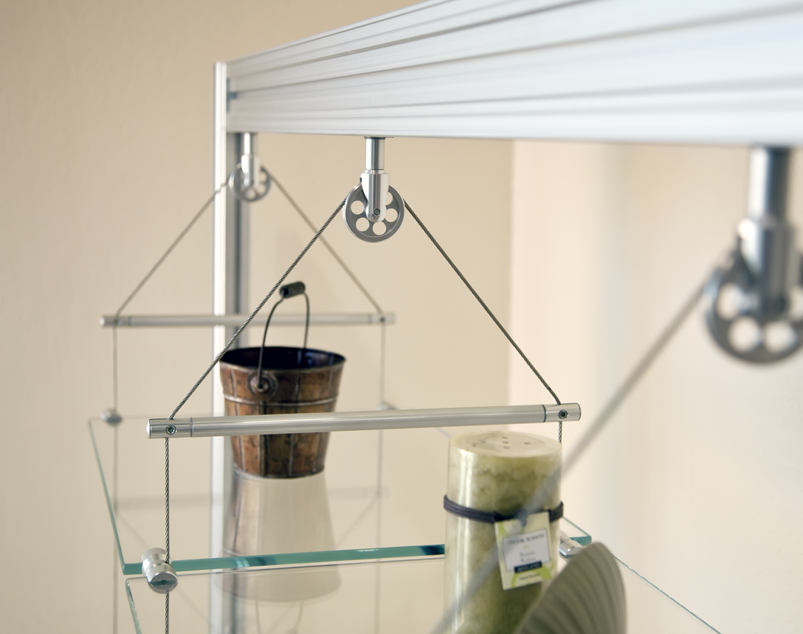 Close-up of glass shelves suspended with wire, pulley hardware, and metal support rods.