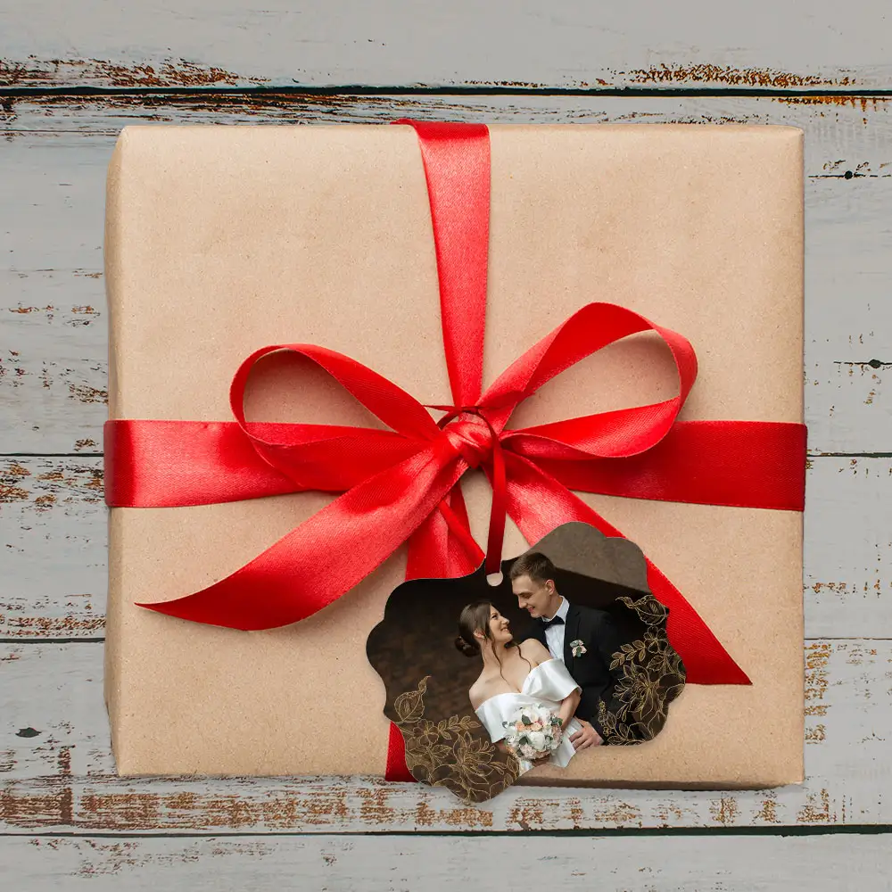Custom photo ornament featuring a couple's wedding portrait with gold floral accents, attached to a red ribbon on a kraft-wrapped gift.