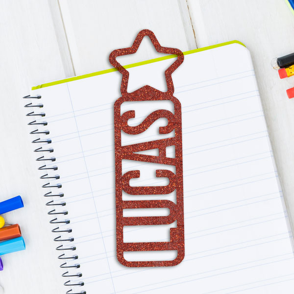 Cast acrylic glitter sheet cut into a bookmark with the name Lucas and a star on top. Bookmark sitting on notebook.