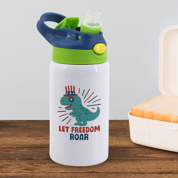 white kids tumbler with a blue and green lid with a patriotic dinosaur and the text let freedom roar printed on it. tumbler is sitting on a table next to lunch