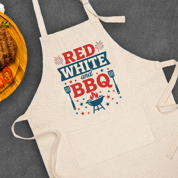 Linen apron with red and blue patriotic design that says red white and BBQ sitting on black table next to burger plate