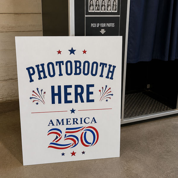 white sign with text Photobooth here America 250 sitting in front of photo booth