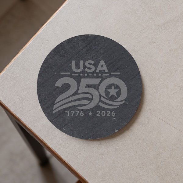 round black slate coaster sitting on a table with USA 250 engraved in gray