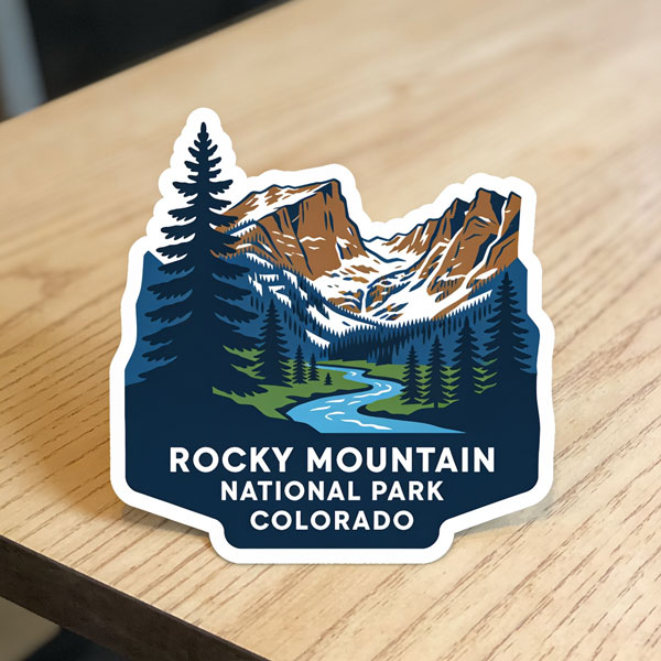 Sticker on a desk with mountains and a river surrounded by trees that says Rocky Mountain National Park Colorado