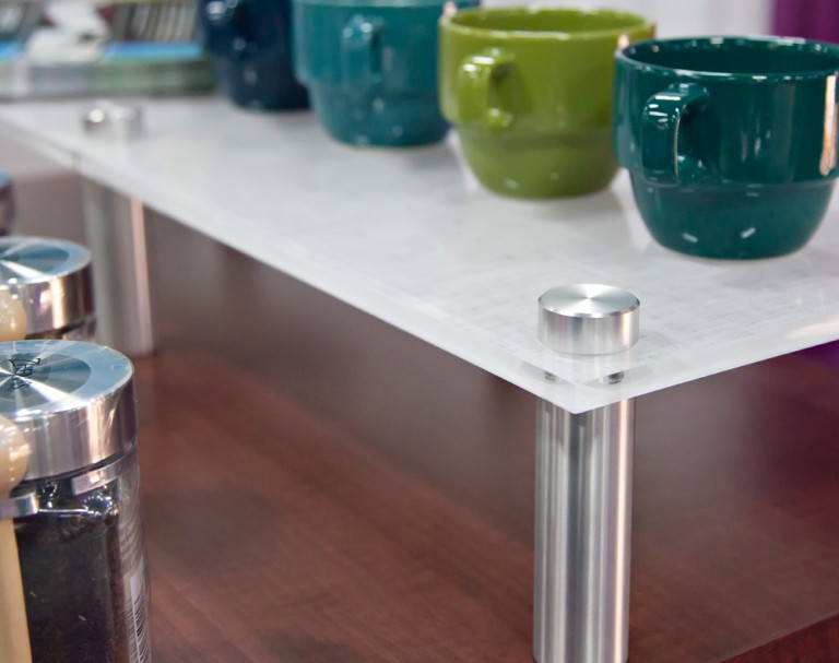 Close-up of a frosted shelf raised on metal standoff supports with mugs displayed on top.