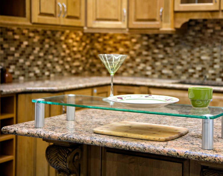 Glass shelf raised on metal standoffs on a kitchen island counter.